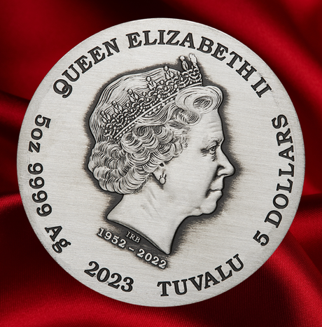 A circular silver-toned coin or medallion featuring Queen Elizabeth II in profile, with the text 'QUEEN ELIZABETH II', '5 DOLLARS', '502 999 Ag', '2023', and 'TUVALU' around the edge. The coin is photographed on a rich red satin fabric background.