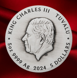 A round silver-toned commemorative coin or medallion featuring a profile portrait of King Charles III, with engraved text reading 'KING CHARLES III', 'TUVALU', '5 OZ 9999 Ag', and '2024 5 DOLLARS', set against a draped red fabric background.