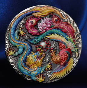 A round silver-toned metal medallion featuring a detailed relief design of a blue dragon and a red phoenix surrounding a pink peony, set against a dark blue satin background.