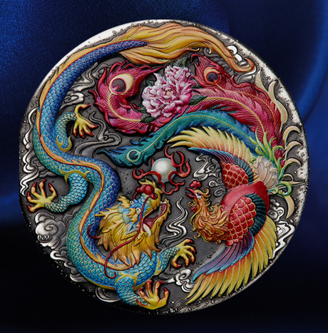A round silver-toned metal medallion featuring a detailed relief design of a blue dragon and a red phoenix surrounding a pink peony, set against a dark blue satin background.