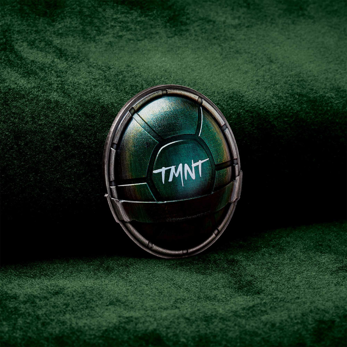 Metallic green object with 'TMNT' text on a dark green background