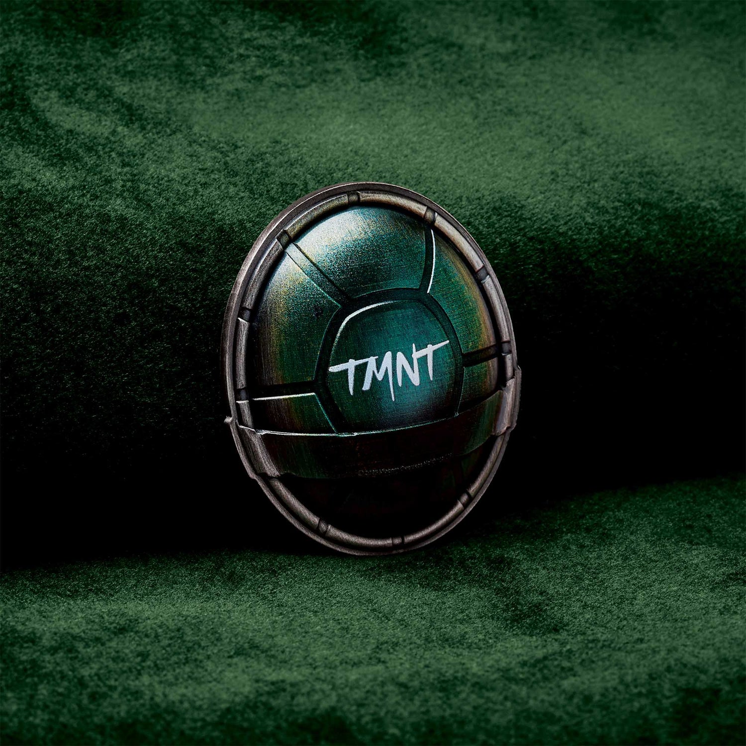 Metallic green object with 'TMNT' text on a dark green background