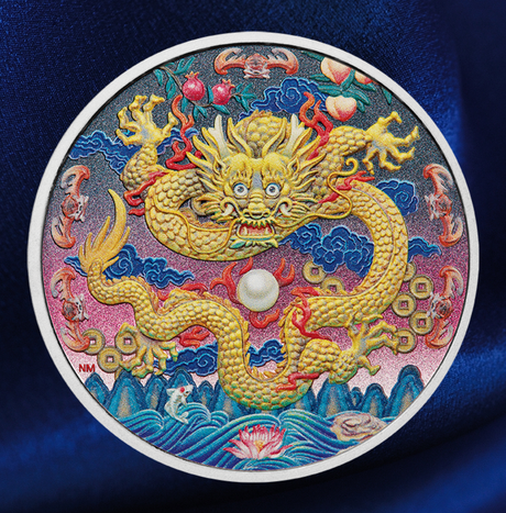 A circular collectible coin featuring a detailed Chinese dragon design, displayed on a dark blue satin fabric background. The coin has a white border and is decorated with a golden dragon, blue clouds, red fruits, and a white pearl-like center.
