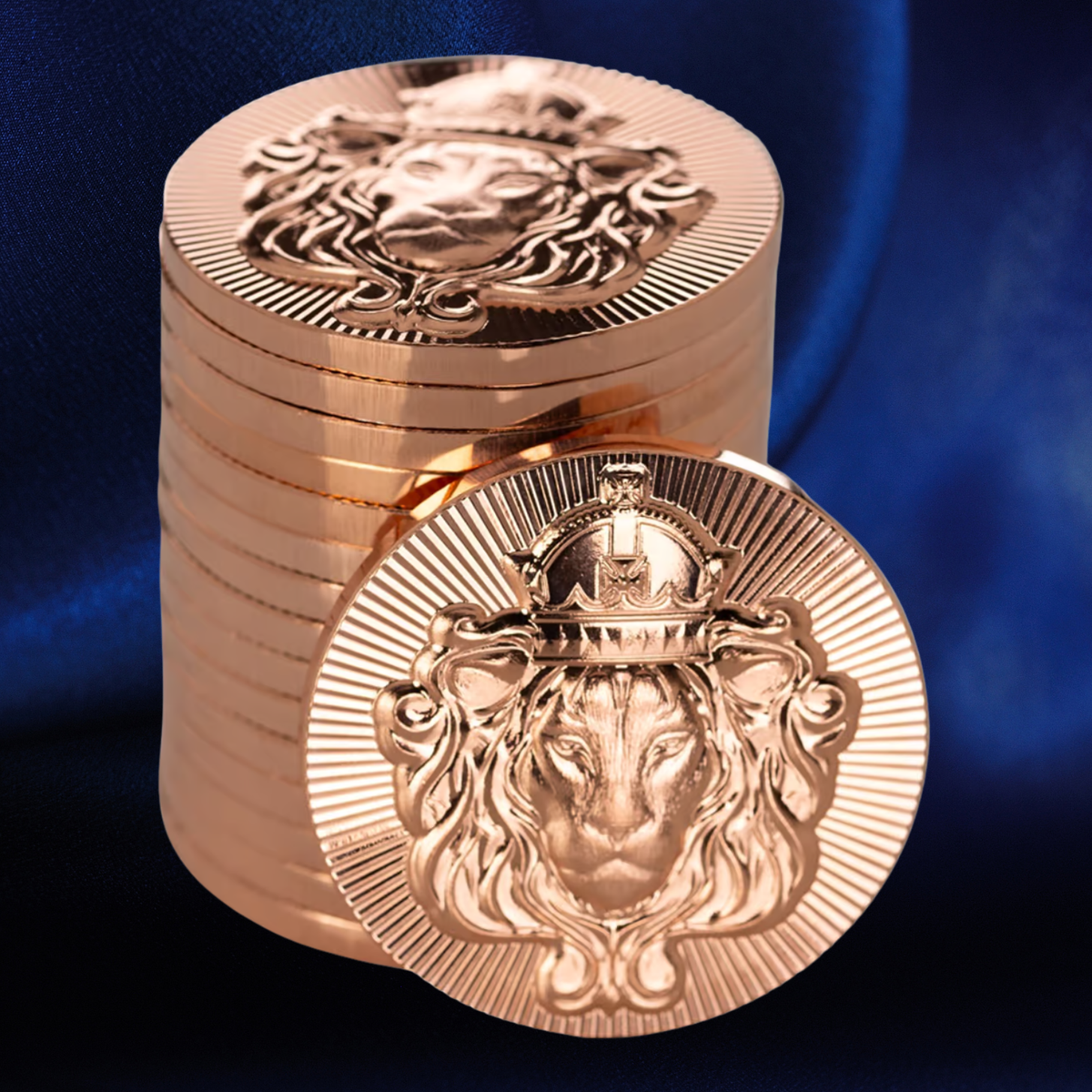 A stack of metallic rose gold coins, with one coin in the foreground displaying an embossed lion head design with a crown, set against a dark blue satin fabric background.