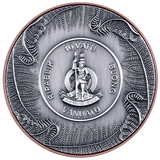 Silver coin with intricate designs and text, featuring a central emblem and surrounding patterns.