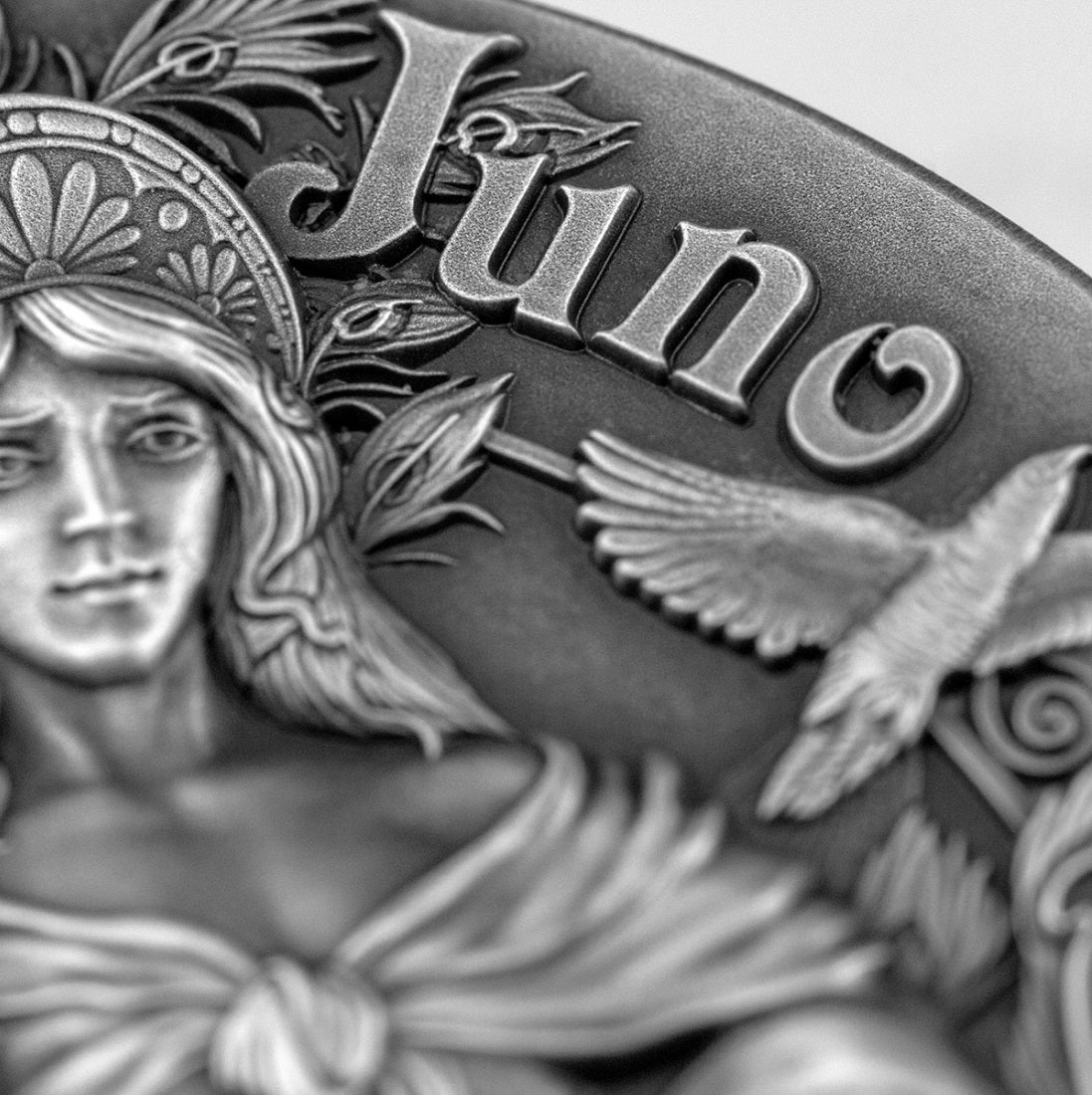  close-up photo of the antique silver coin highlighting the face of the goddess Juno. Her classical profile features a focused expression, an detailed headpiece, and sculpted hair textures accented by deep gray shadows from the antique finish.