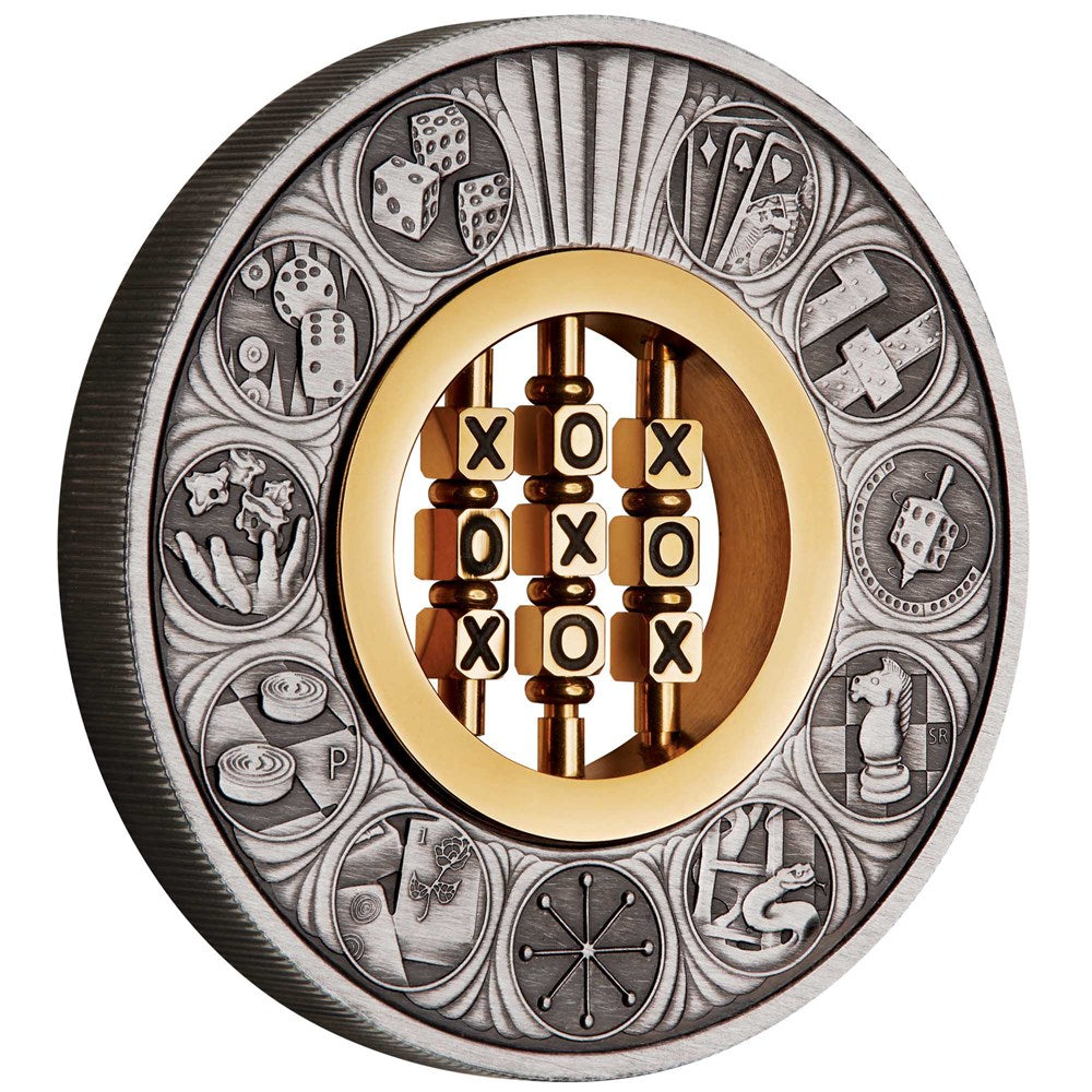 Reverse design of the 2022 2oz silver antiqued coin by The Perth Mint. The outer ring showcases highly detailed matte silver engravings of classic games—including playing cards, dominoes, a spinning die, chess pieces, snakes and ladders, mahjong tiles, backgammon, and knucklebones. Deep gray shadows from the antique finish highlight the details. The centerpiece holds a functioning, 24-carat gold-plated stainless steel 'Noughts and Crosses' game insert with turning cubes.